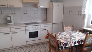 Eine Küche mit Fliesenboden, einer Kaffeemaschine, einem Herd, einem Kühlschrank und einem Esstisch mit Stühlen.