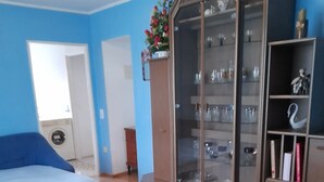Ein Wohnzimmer mit einer Couch, einem Esstisch mit einer Schüssel, einem Schrank mit Gläsern und einem Bücherregal.