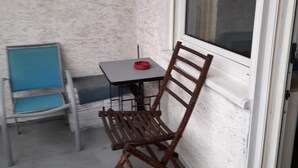Ein kleiner Außenbereich mit Tisch und zwei Stühlen, ein blauer und ein brauner, an einer strukturierten Wand.