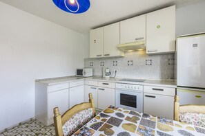 Una cocina compacta con armarios blancos, microondas, cafetera y refrigerador.