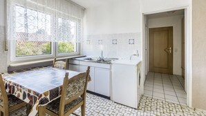 Cocina compacta con una mesa y sillas, un lavamanos y una puerta que da a otra habitación.