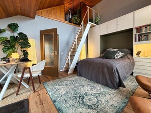 A bedroom with a bed, a desk, a chair, a staircase, and a bookshelf.