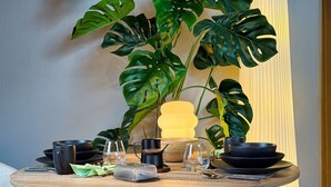 A round wooden table with black and clear glassware, a yellow lamp, and a large green plant in the background. - Eichenwald Studio with Mountain View, Fireplace, Balcony, and Wi-Fi (Bad Herrenalb)