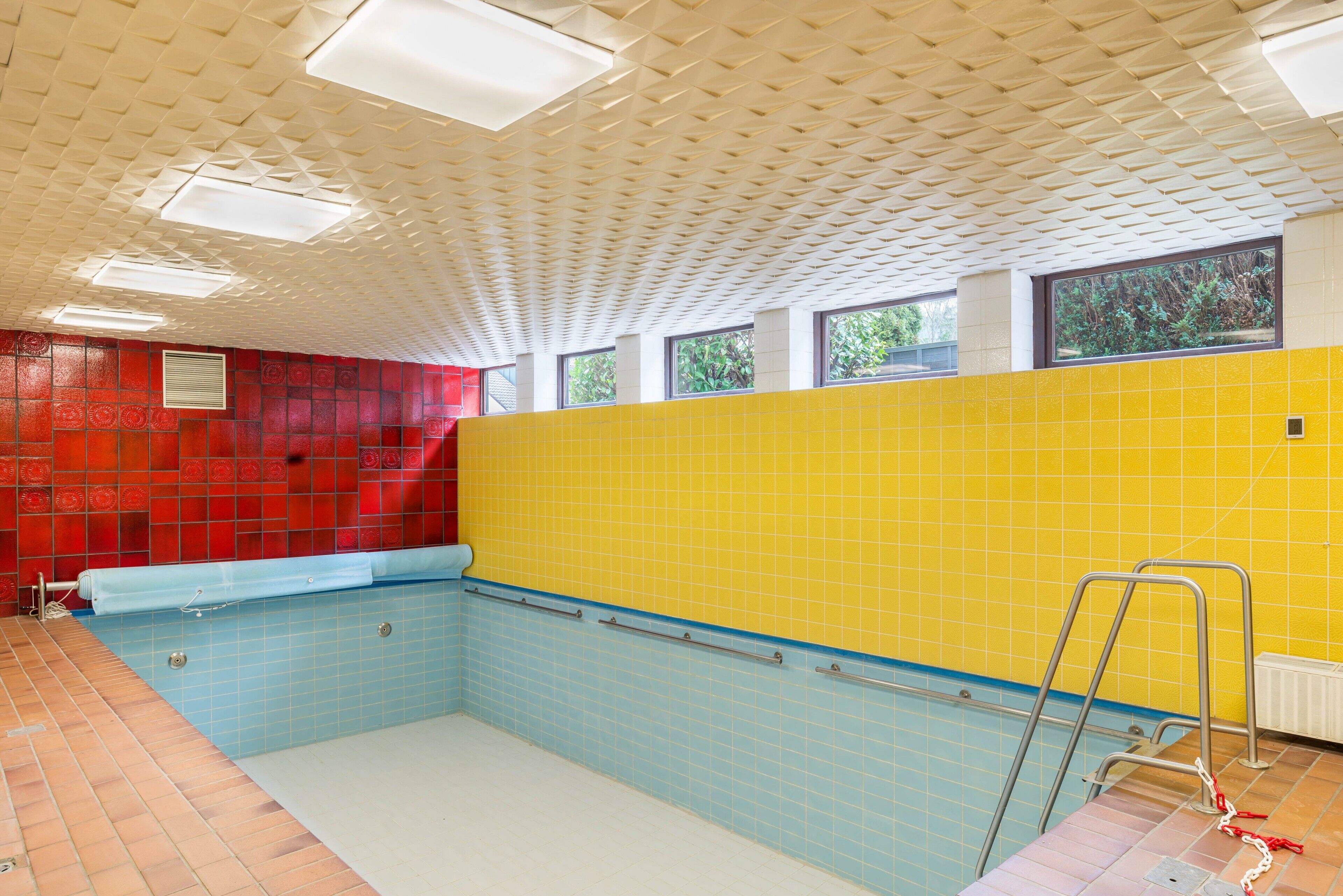 Ein Innenpool mit gefliestem Boden, einer roten und gelben Wand und einer Decke mit geometrischem Muster.