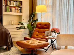 A modern living room with a leather armchair, a bookshelf, a floor lamp, and a side table with a vase of flowers.