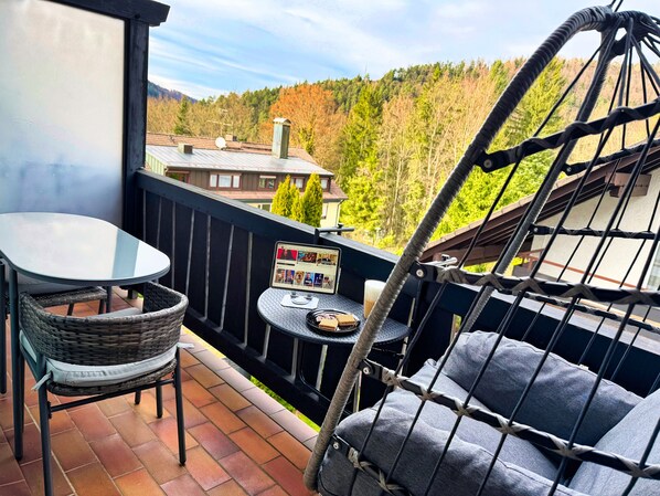 A balcony with a hanging chair, a table, and a small TV.