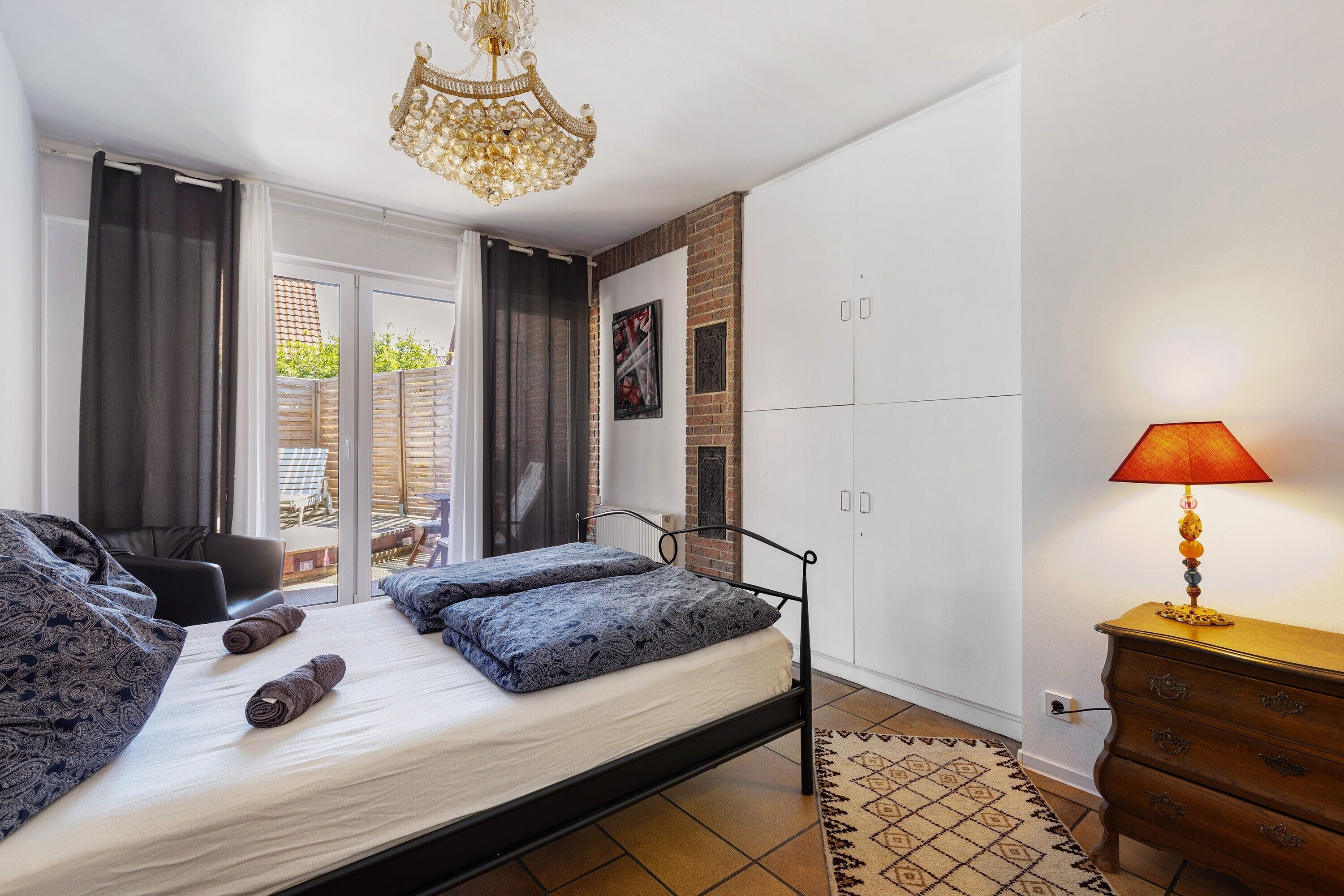 Une chambre à coucher avec un lit, une commode, une lampe et une vue par la fenêtre.