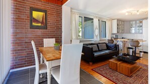 Una sala de estar moderna con una mesa de comedor, sillas blancas, un sofá negro y una zona de cocina al fondo.