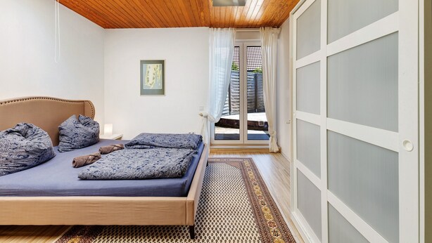 Un dormitorio con cama, techo de madera, puerta con paneles de vidrio esmerilado y alfombra estampada.