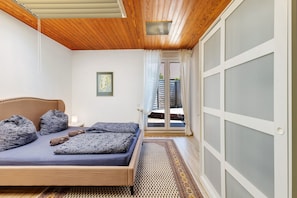 Un dormitorio con cama, techo de madera, puerta con paneles de vidrio esmerilado y alfombra estampada.