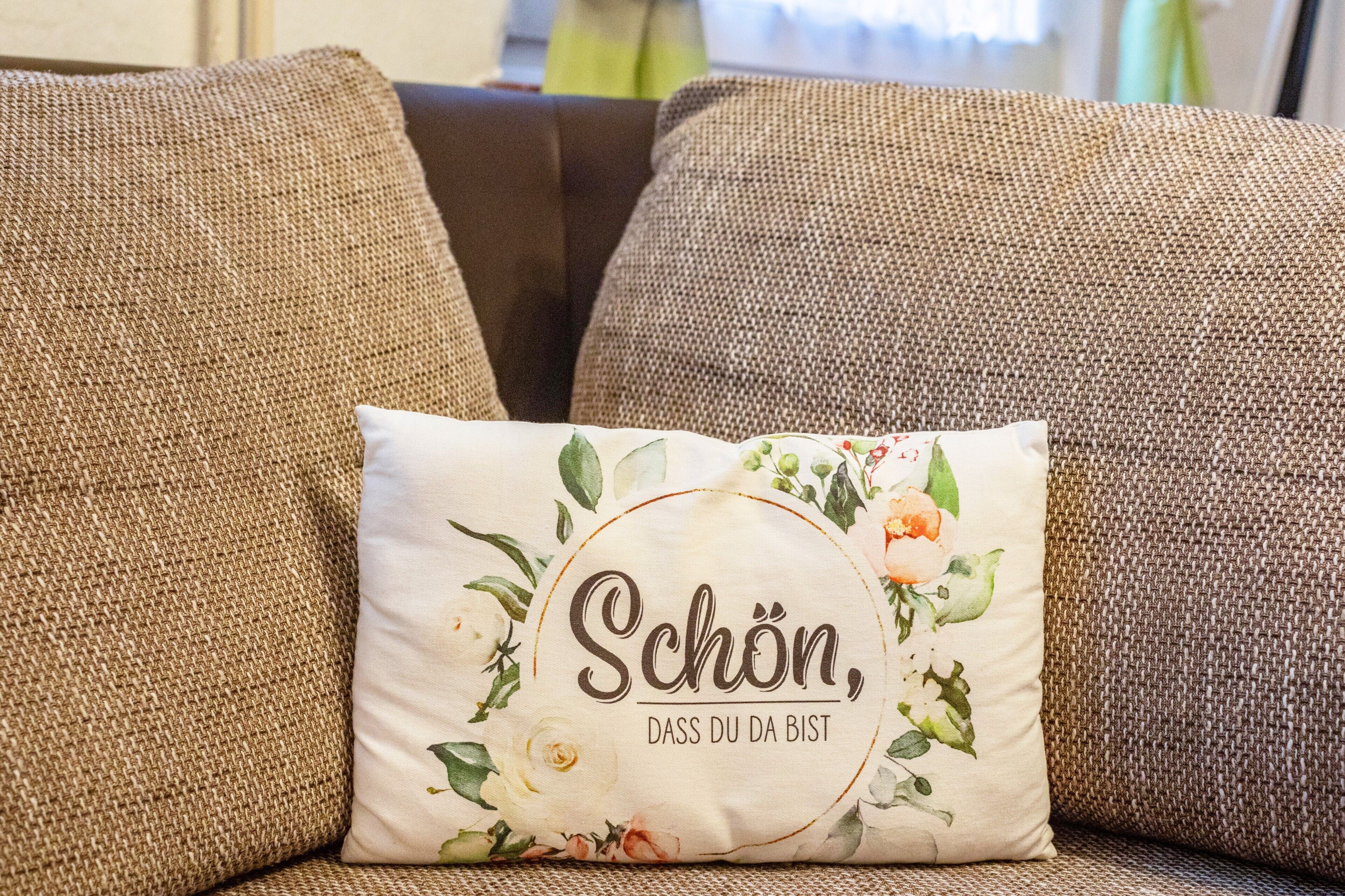 Een bank met een kussen met bloemenmotieven en tekst.
