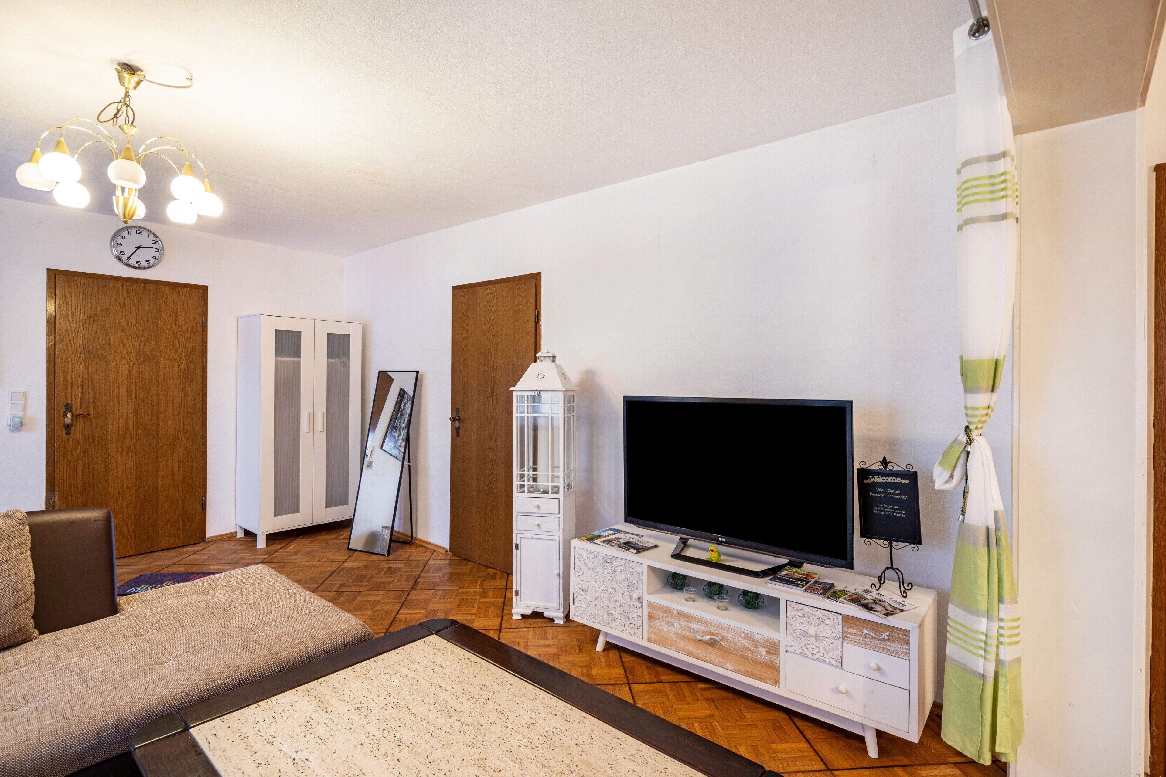A living room with a sofa, TV, white cabinet, wooden door, and a clock on the wall.