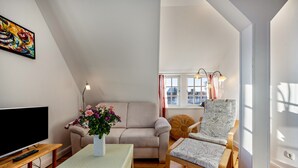 Una sala de estar con un sofá, una silla, una mesa con un florero, un televisor y una ventana con cortinas.
