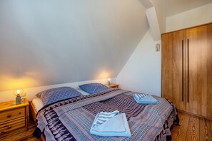 Quarto com cama, guarda-roupa de madeira, mesas de cabeceira e uma luminária.