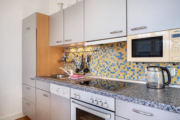 A modern kitchen with white cabinets, a granite countertop, a microwave, and a kettle.
