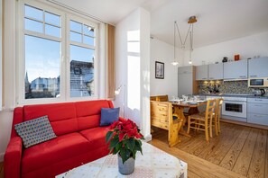 A modern living room with a red sofa, a dining area with wooden furniture, and a kitchen with white cabinets and a tiled backsplash.