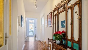 A hallway with wooden flooring, a bench, a mirror with a decorative frame, and a door leading to another room. - Apartment 'Haus Übersee Wohnung Fidji' with Private Terrace, Shared Garden and Wi-Fi (Lübeck-Travemünde)