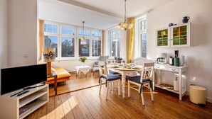 A well-lit room with a dining table, chairs, a television, and a cabinet with glass doors. - Apartment 'Haus Übersee Wohnung Fidji' with Private Terrace, Shared Garden and Wi-Fi (Lübeck-Travemünde)