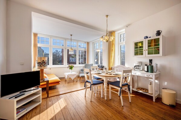 A well-lit room with a dining table, chairs, a television, and a cabinet with glass doors.
