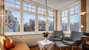 A room with large windows, a sofa, two chairs, a small table with a vase, and a hanging light fixture. - Apartment 'Haus Übersee Wohnung Fidji' with Private Terrace, Shared Garden and Wi-Fi (Lübeck-Travemünde)