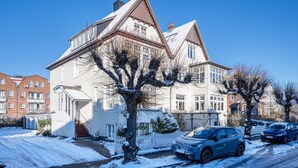 A two-story house with a snow-covered driveway and parked cars. - Apartment 'Haus Übersee Wohnung Fidji' with Private Terrace, Shared Garden and Wi-Fi (Lübeck-Travemünde)
