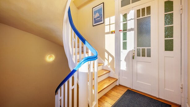 A staircase with white railings and a blue handrail leading to a door with frosted glass panels. - Apartment 'Haus Übersee Wohnung Fidji' with Private Terrace, Shared Garden and Wi-Fi (Lübeck-Travemünde)