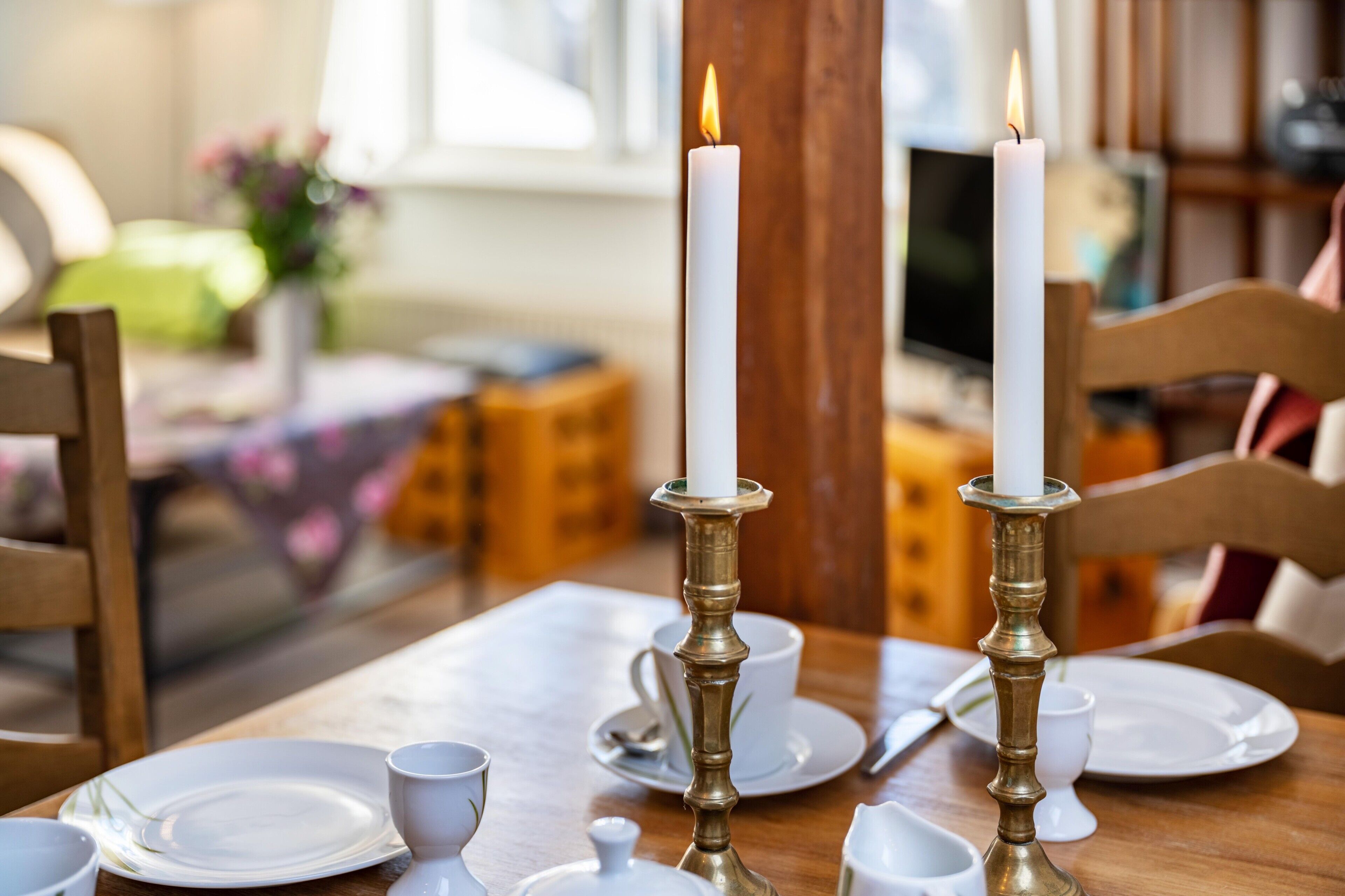 Una mesa de comedor con platos blancos, tazas y un candelabro con velas encendidas.