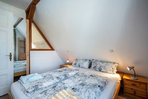 A bedroom with a sloped ceiling, a bed with patterned bedding, two bedside tables with lamps, and a wooden wardrobe.