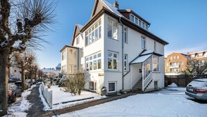 Una casa de dos pisos con entrada principal, una escalera visible y un camino de entrada cubierto de nieve.