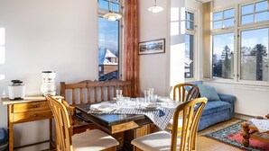 A dining area with a table set for four, a wooden desk with a coffee maker, and a blue sofa in the corner.