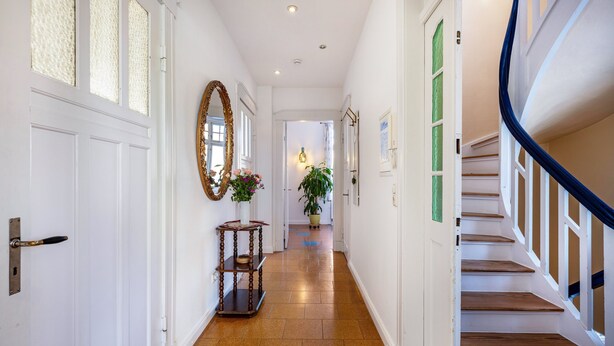 A hallway with a wooden staircase, white doors, and a mirror.