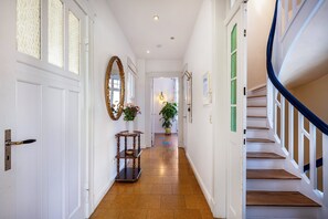Un couloir avec un escalier en bois, des portes blanches et un miroir.