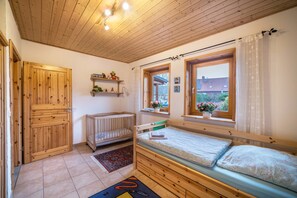 Quarto com teto de madeira, berço, cama e janela.