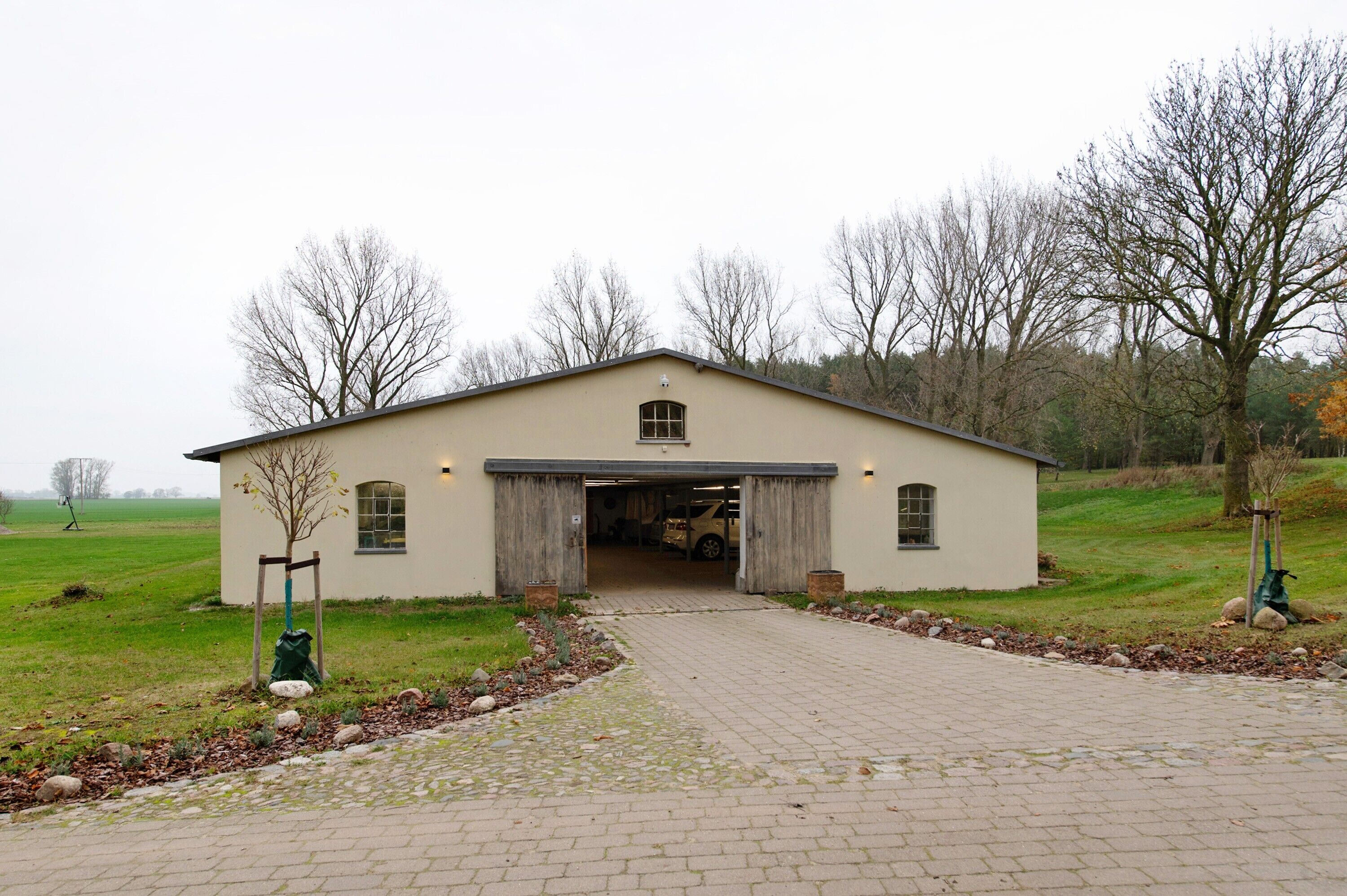 A single-story building with a garage door open, surrounded by a paved driveway and a grassy field.