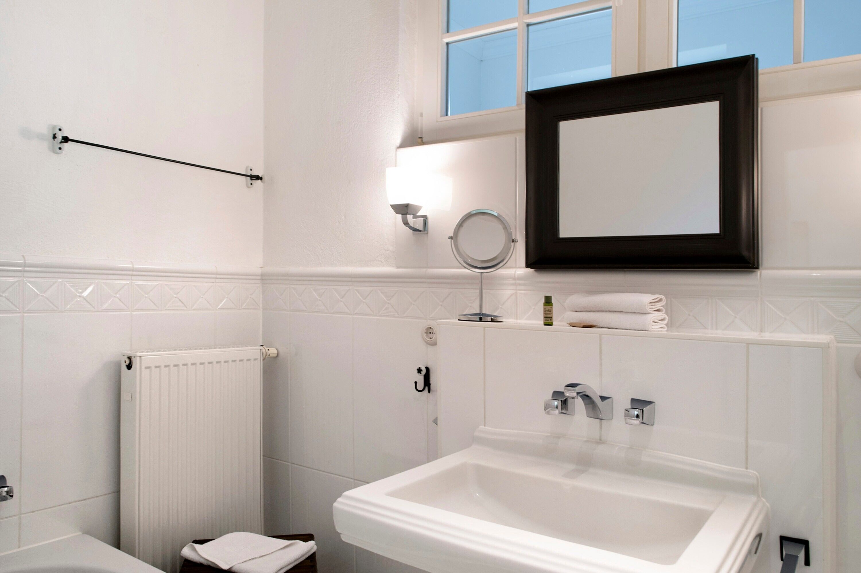 Een badkamer met een witte wasbak, een spiegel, een handdoekrek en een raam.
