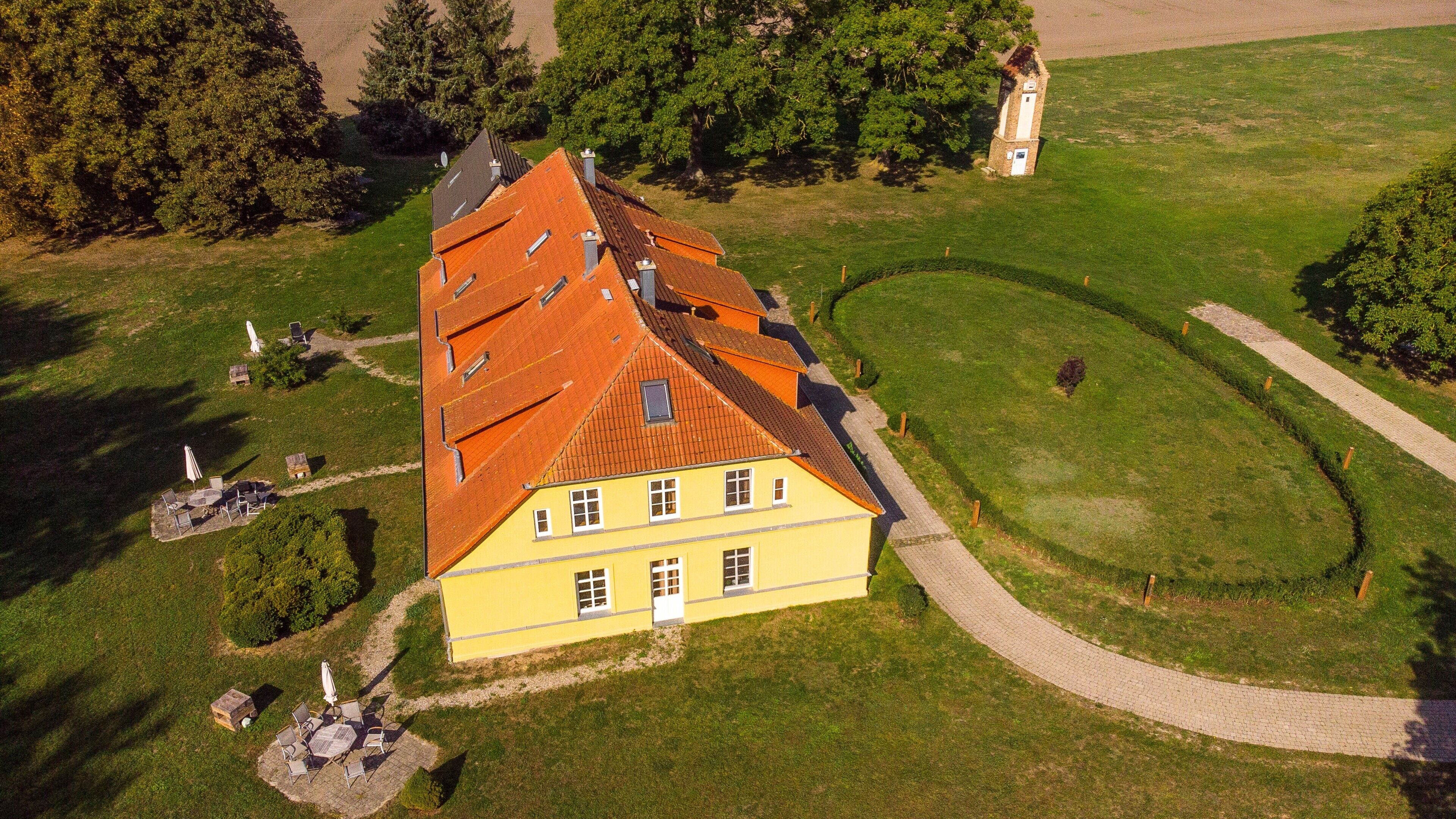 A large yellow building with a sloped roof, surrounded by a well-maintained lawn and a paved path.