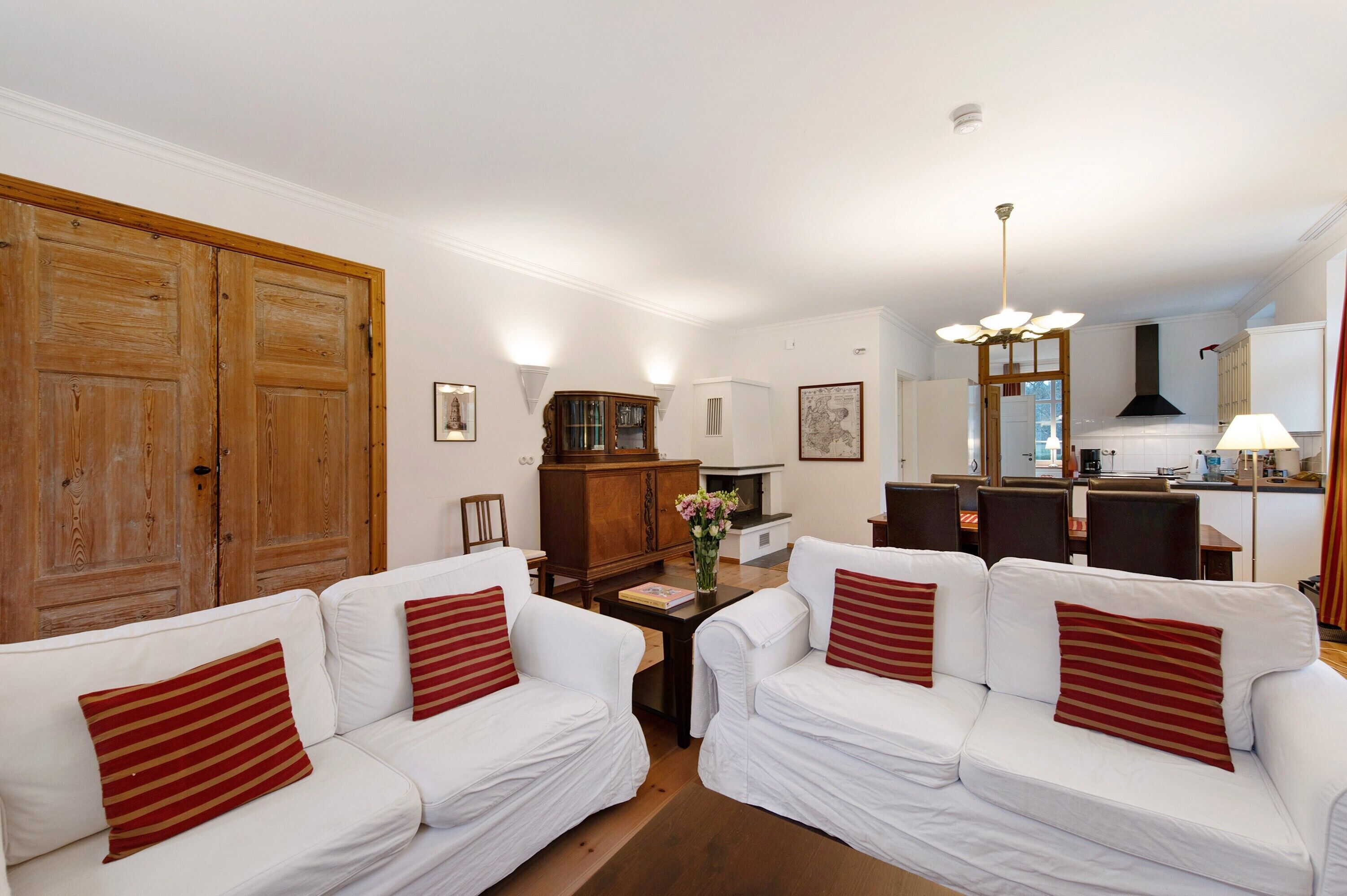 A living room with two white sofas, a wooden cabinet, a dining area, and a kitchen in the background.