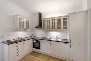 Una cocina con armarios blancos, horno negro, campana extractora de acero inoxidable y encimera con pileta.