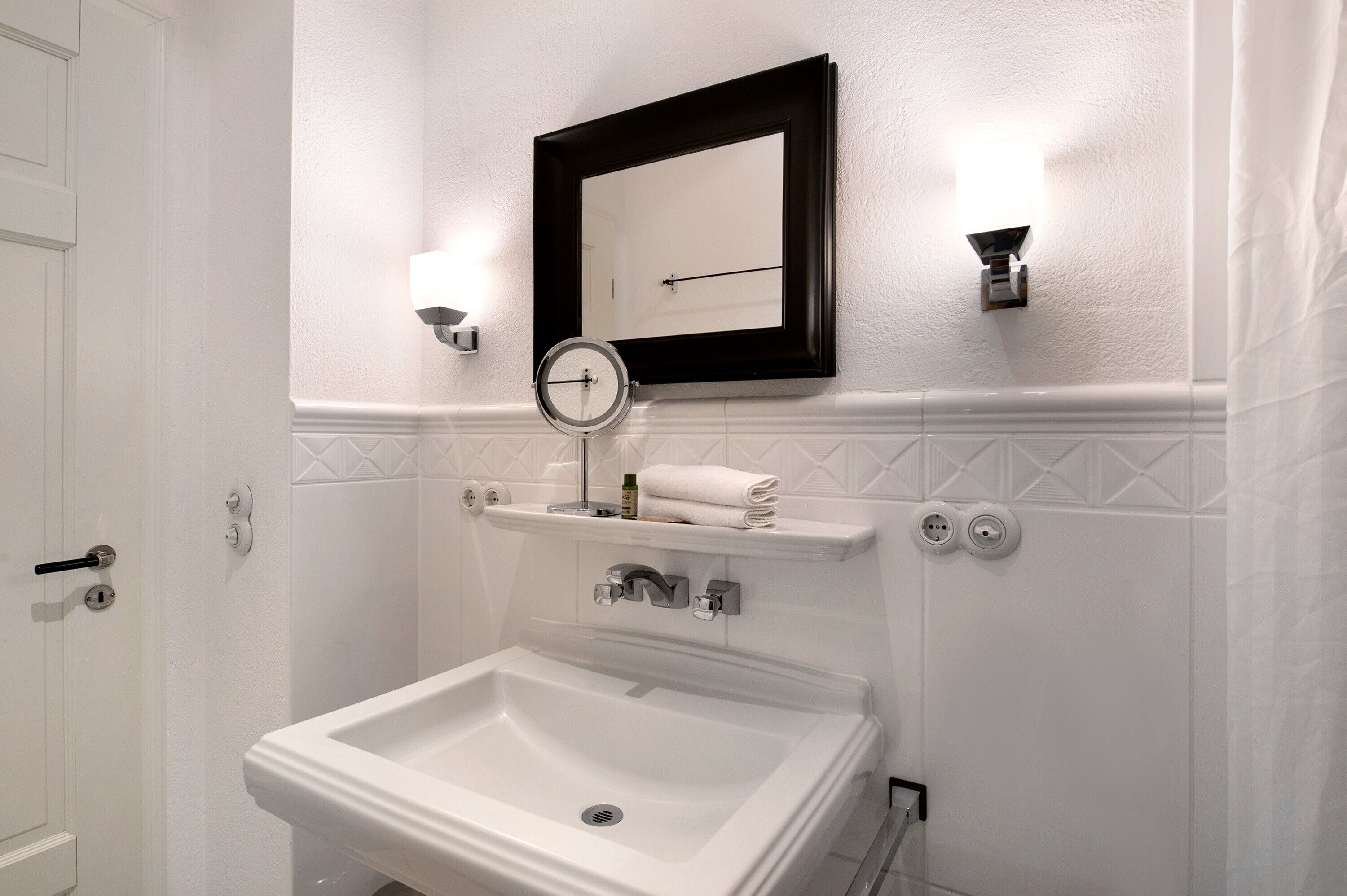Un baño con lavamanos blanco, un espejo y un perchero para toallas.