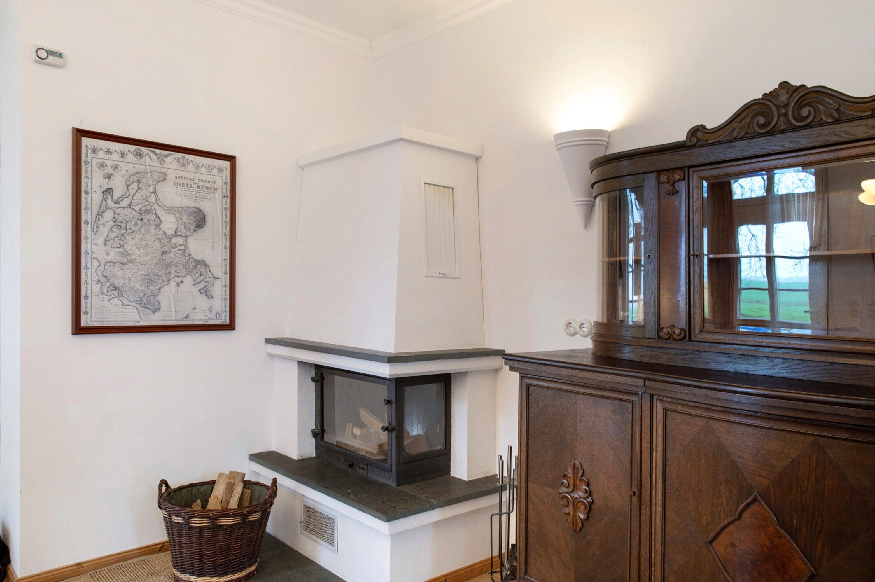 A room with a fireplace, a wooden cabinet, a wicker basket, and a framed map on the wall.