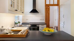 Une cuisine avec des armoires blanches, une hotte noire, un bol de citrons et un plateau contenant divers ustensiles de cuisine.