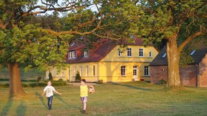 Une maison à la façade jaune, avec une partie en briques et un toit rouge.