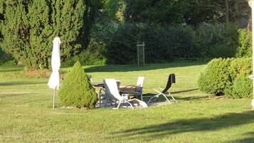 An outdoor seating area with a table and chairs, surrounded by greenery and trees.
