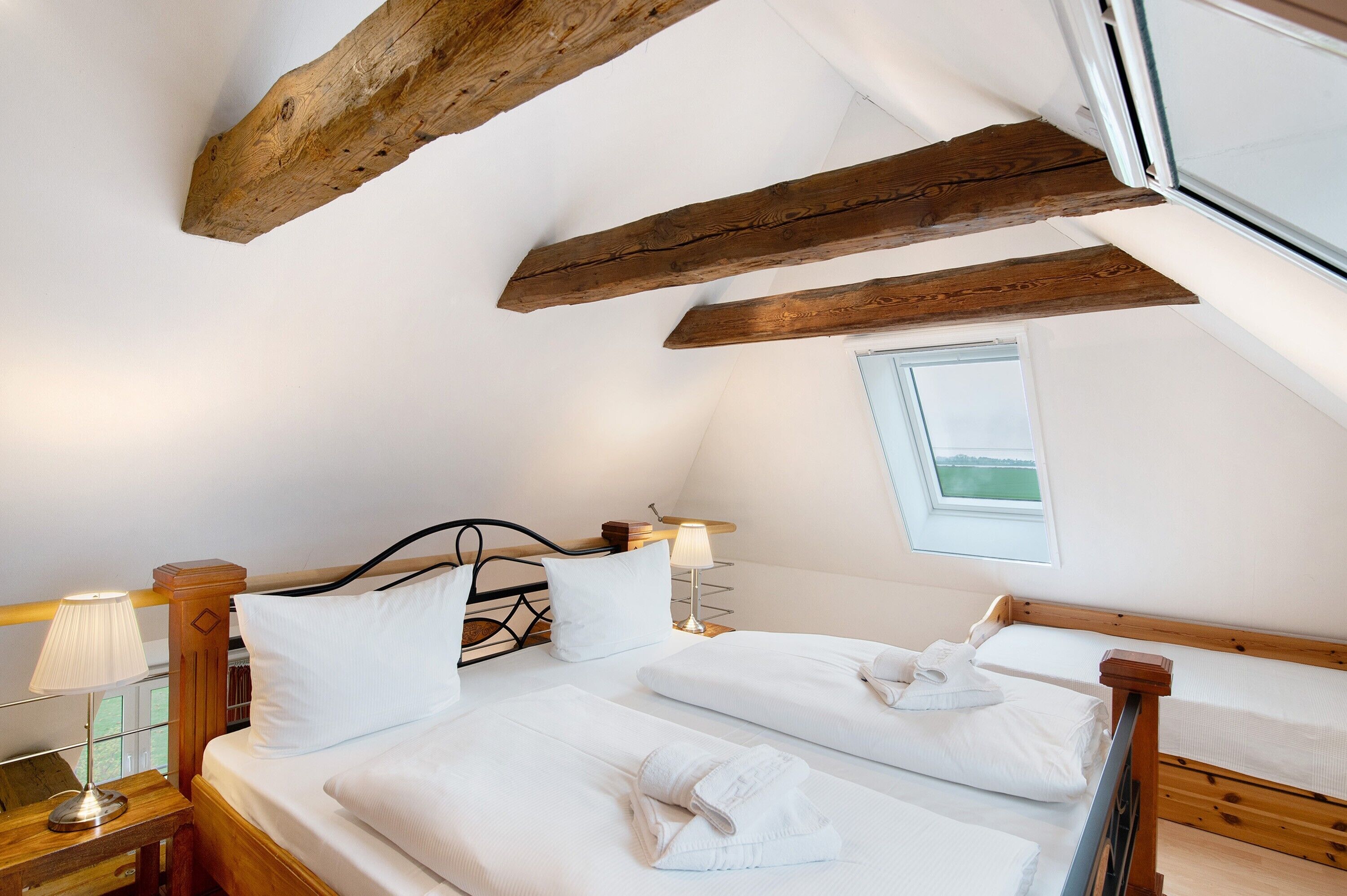 A bedroom with two beds, wooden beams, a window, and a lamp.