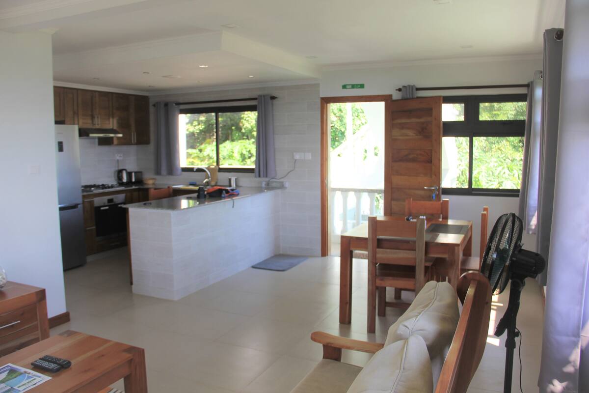 A modern kitchen with a central island, wooden dining table, and chairs.