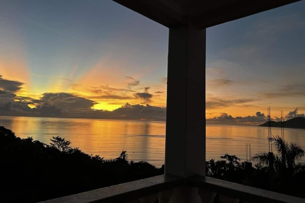 A sunset view from a balcony overlooking a calm body of water with distant landforms.
