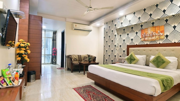 Una habitación de hotel con una cama, un escritorio con aperitivos, una silla, un ventilador de techo y una pared con diseño.