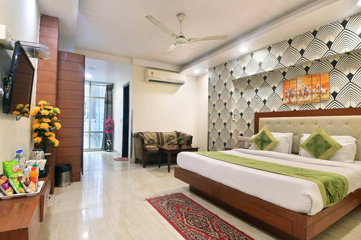 Una habitación de hotel con una cama, un escritorio con aperitivos, una silla, un ventilador de techo y una pared con diseño.