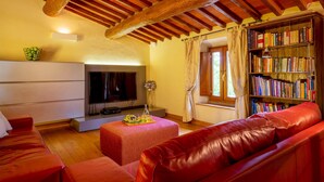 Una sala de estar acogedora con un sofá de cuero rojo, un televisor de pantalla plana, una estantería y una ventana con cortinas.