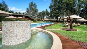 Una piscina con mosaicos, rodeada por una terraza de madera y sillas de descanso.